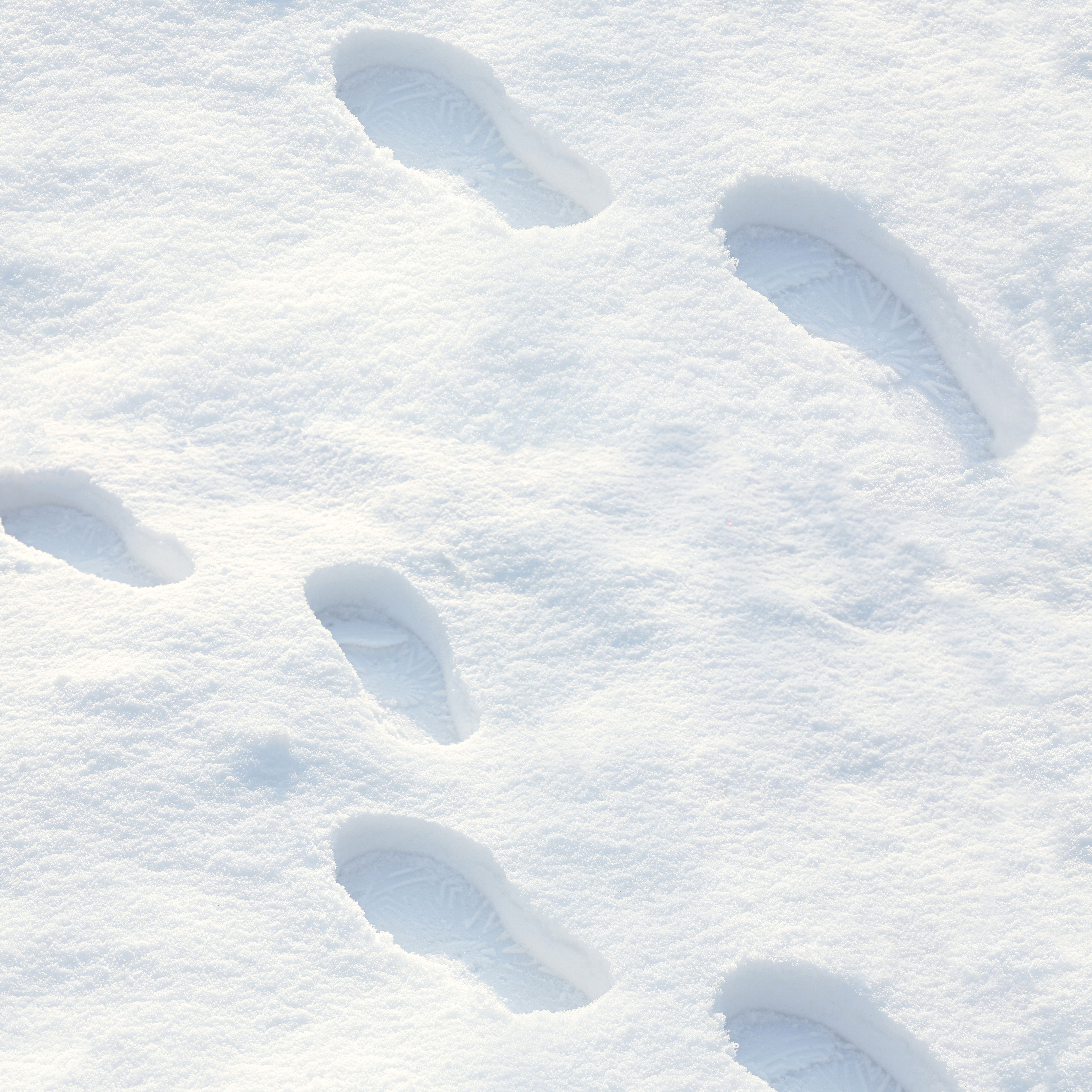 Mehrere Schuhabdrücke im frischen Schnee zeigen Profilspuren als Hinweis auf winterfeste Schuhe mit griffiger Sohle.