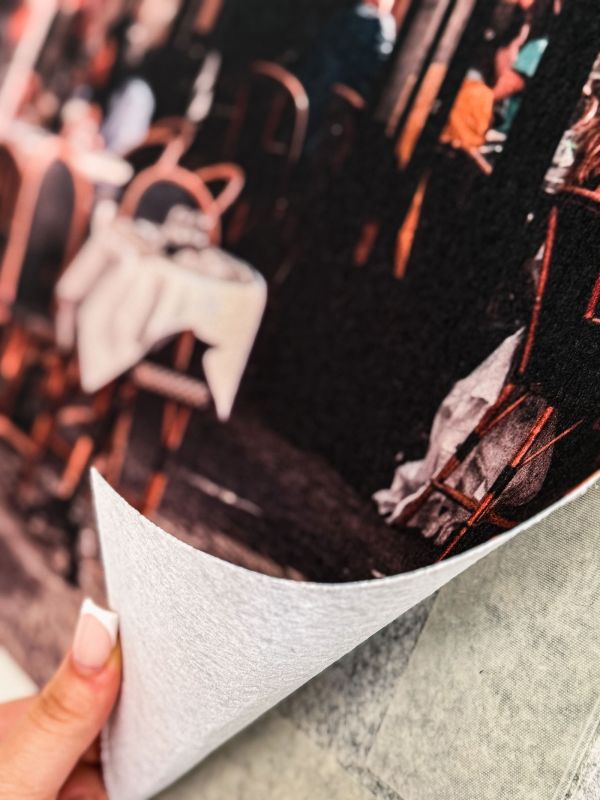 Close-up of Wand + Boden Druck polyester wall and floor graphic with “Puzzle bunt” motif, showing a hand lifting the corner of the digitally printed covering for easy installation