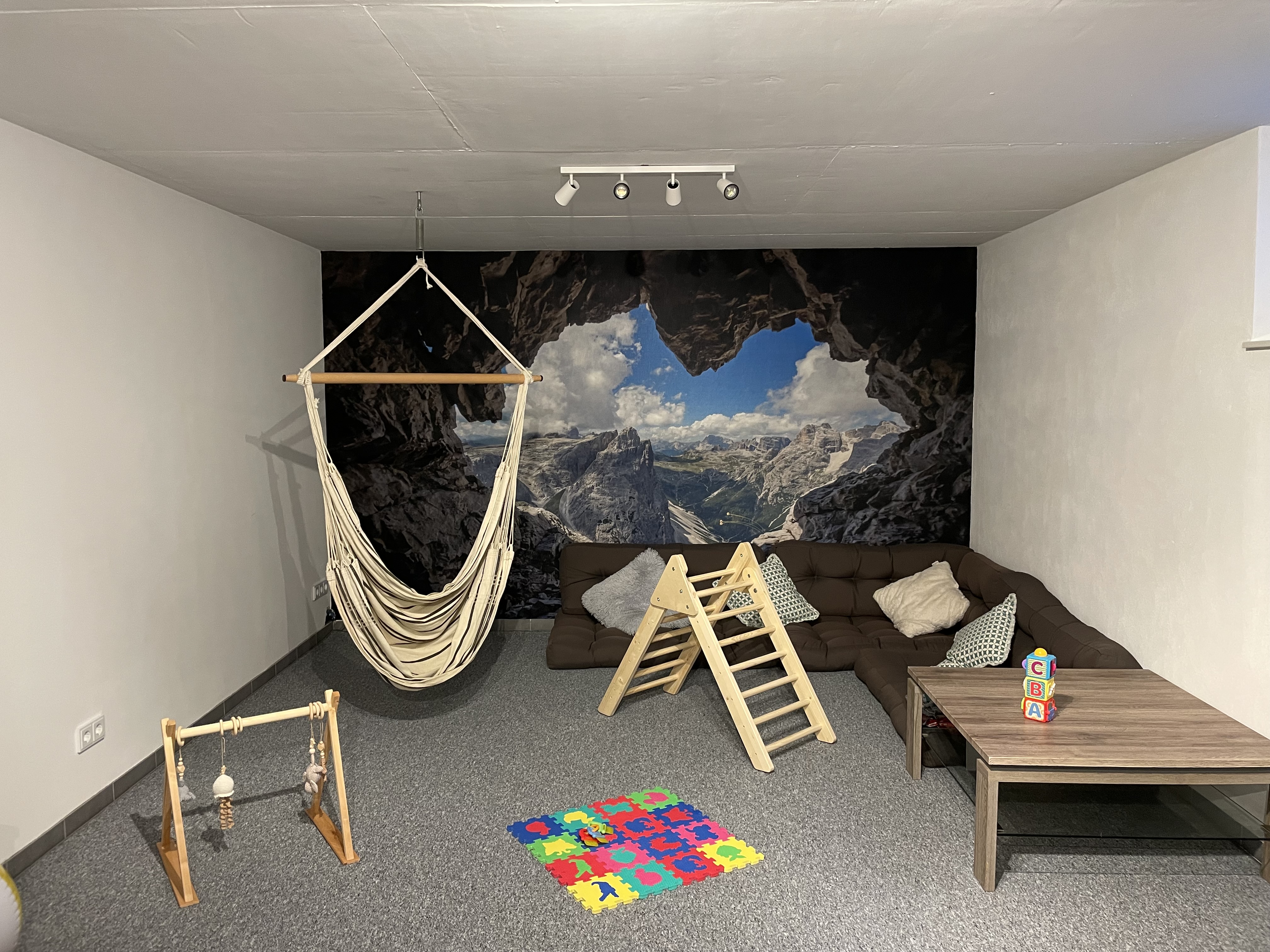 Spielzimmer mit Hängesessel, Kletterdreieck, Sofa und großer Fototapete mit Berglandschaft als Wandgestaltung
